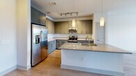 Located at 300 District Dr in Asheville, NC, this one-bedroom, one-bathroom unit offers a well-designed open-concept layout that maximizes its comfortable footprint. The kitchen and living area flow seamlessly together, anchored by a large granite-topped island with an undermount sink and pendant lighting overhead. The kitchen is outfitted with gray shaker-style cabinetry, a classic white subway tile backsplash, stainless steel appliances including a French door refrigerator, electric range, and built-in microwave, plus a dedicated pantry for added storage. Light hardwood-style flooring runs throughout the main living areas, complemented by ceiling fans that enhance airflow and comfort. The living room receives abundant natural light through large windows with outdoor views. The spacious bedroom features plush carpeting, a ceiling fan, and generous window exposure. Three closets provide ample storage, including a walk-in closet with built-in wire shelving. The bathroom features a granite-topped vanity with gray cabinetry and wood-style flooring. A dedicated laundry area adds everyday convenience. Clean white walls and neutral finishes throughout create a bright, modern, and move-in-ready atmosphere.