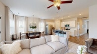 This two-story home offers a thoughtfully designed layout that balances open communal living with comfortable private spaces. The main floor is anchored by a bright, open-concept living, dining, and kitchen area. Light wood-look flooring runs throughout, complementing the home's neutral, warm color palette. The kitchen is outfitted with white shaker-style cabinetry, stainless steel appliances including a French door refrigerator and built-in microwave, a white quartz island with bar seating, and pendant lighting. The adjacent dining area benefits from abundant natural light through large windows dressed in linen curtains, centered beneath a modern chandelier. The living area features a ceiling fan and flows seamlessly into the rest of the main floor. A dedicated sitting room provides a quieter retreat with natural light and neutral finishes. Upstairs, multiple bedrooms offer restful accommodations with soft tones and ample closet space. The primary bathroom includes a glass-enclosed walk-in shower and wood-look flooring. A dedicated laundry room with a full-size washer and dryer adds everyday convenience. A staircase with wood-toned treads and a white balustrade connects both floors, establishing a clean and cohesive aesthetic throughout the home.