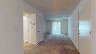 This single-floor residence in Decatur, Georgia, offers a functional and straightforward layout across several interconnected spaces. The living area serves as the central gathering space, finished with wall-to-wall neutral carpet and topped with a textured ceiling. A large sliding glass door fitted with vertical blinds allows natural light to filter in while providing outdoor access. White walls throughout contribute to a clean, open atmosphere.

The galley-style kitchen is efficiently arranged with white cabinetry lining both sides, providing ample storage. Wood-look flooring runs underfoot, complementing the white appliances, which include a coil-top electric range, dishwasher, and full-size refrigerator. An overhead range hood adds practical ventilation above the stove.

The bedroom is a comfortably sized, carpeted room with a window fitted with horizontal blinds that introduces natural light. A ceiling vent and floor register indicate the presence of a central HVAC system. The room connects conveniently to adjacent spaces via a hallway.

The bathroom features wood-look flooring, a white vanity with cabinet storage beneath a light countertop, and a tub-shower combination. The overall design of the unit is utilitarian and move-in ready, suited for comfortable everyday living.