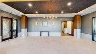 Located at 1100 Knotts Pointe Ln in Suffolk, Virginia, this single-floor commercial space offers a polished, contemporary design with thoughtful finishes throughout. The grand lobby immediately impresses with large-format light tile flooring, warm wood accent panels, and a striking multi-globe pendant chandelier suspended from a richly textured dark ceiling with integrated ambient lighting. Floor-to-ceiling glass curtain walls and double glass entry doors flood the space with natural light while offering views of the surrounding landscape. Paired leather accent chairs provide a welcoming seating area near the entrance.

From the lobby, multiple well-appointed hallways extend throughout the space, lined with light wood-tone flooring, dark baseboards, and curated artwork — including nature-themed pieces that lend a refined, professional atmosphere. The hallways lead to various private rooms and connect the facility's functional areas seamlessly.

Two modern bathrooms feature large-format tile walls and floors, wood-grain stall partitions, matte black hardware and fixtures, and built-in dispensers for a clean, upscale appearance. A secondary entrance with glass doors and wood-look flooring provides additional access to the exterior. Throughout, the design balances professional functionality with elevated aesthetics.