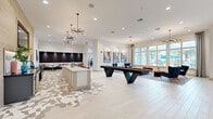 This generously proportioned single-floor amenity lounge delivers a polished, contemporary atmosphere designed for both relaxation and social engagement. Light-toned hardwood flooring extends throughout the open-plan layout, complemented by an eye-catching geometric tile inlay that anchors the central gathering zone. The space is organized into distinct yet seamlessly connected areas, each thoughtfully furnished and lit.

A central bar-style counter with dark fluted paneling serves as a visual anchor, while a full-length community table with leather swivel seating provides a dedicated space for shared activities or casual dining. A striking shuffleboard table positioned nearby adds a recreational focal point. Stylish sputnik-style chandeliers and pendant lighting enhance the sophisticated aesthetic overhead.

One end of the lounge features a dramatic wood-paneled ceiling with an integrated flat-screen TV and gray lounge chairs, creating an intimate media nook. Bold horizontal gold-and-white striped wall accents add a playful design element nearby. A separate lounge area with mid-century modern furniture is bathed in natural light from floor-to-ceiling windows draped in sheer linen curtains, offering direct views of a vibrant outdoor pool area. Colorful artwork, richly upholstered seating, and carefully curated décor complete the resort-inspired ambiance of this exceptional communal space.