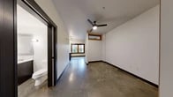 Located in Portland's vibrant NW Irving Street corridor, this single-floor space showcases a thoughtfully designed modern interior with a cohesive industrial-contemporary aesthetic. Polished concrete floors run throughout, providing a sleek, durable foundation that ties the entire space together.

The kitchen is a standout feature, outfitted with taupe upper cabinetry, white subway tile backsplash, and a bold navy blue island with crisp white countertops. Stainless steel appliances — including a full-size refrigerator, dishwasher, gas range, and microwave — add a professional touch. A large, wood-framed picture window floods the kitchen and living area with natural light and offers a view of the outdoor greenery, while pendant lighting above the island adds warm ambiance.

The living and sleeping areas feature the same polished concrete flooring, continued white walls, and high transom windows with warm wood framing that bring in additional natural light. A ceiling fan provides year-round comfort.

The bathroom is clean and well-appointed, featuring polished concrete floors, a dark-toned vanity with a white countertop, a framed mirror, a walk-in shower, and tall built-in cabinetry providing ample storage. Black hardware and fixtures throughout the space lend a refined, modern edge to the overall design.