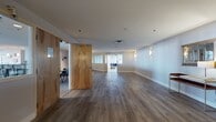 Located at 1278 W Ninth St in Cleveland's vibrant Ohio City neighborhood, this single-floor commercial space offers a well-designed blend of open and private areas suited for professional use. The main corridor features durable wood-look flooring, clean white walls with sconce lighting, and natural flow between zones. A spacious central lounge is carpeted and furnished with neutral sofas and accent chairs arranged around low tables, bordered by a distinctive row of interior clerestory windows that allow light to pass between areas. Adjacent seating nooks offer blue upholstered sofas and chairs on polished concrete floors, with exterior windows providing views of the surrounding Cleveland skyline. A fully equipped kitchen anchors one corner of the space, highlighted by a stone-clad breakfast bar with pendant lighting, stainless steel appliances, warm wood cabinetry, and a granite countertop. Dedicated meeting rooms with rich hardwood floors and large multi-pane windows deliver abundant natural light and city views, making them ideal for focused work or small group sessions. Throughout, the design balances an open, welcoming atmosphere with defined functional zones, creating a versatile environment well suited for collaborative professional use.