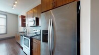 Located on North High Street in Columbus, Ohio's vibrant Short North neighborhood, this single-floor unit offers a well-designed layout with modern finishes throughout. The open kitchen is a standout feature, equipped with stainless steel appliances including a Whirlpool side-by-side refrigerator, electric range, built-in microwave, and dishwasher. Warm-toned wood cabinetry reaching to the ceiling maximizes storage, while dark granite countertops and a tiled backsplash add a polished, contemporary aesthetic. Track lighting illuminates the kitchen and adjoining living area, which features rich, dark hardwood-style flooring that flows seamlessly through the main living spaces. The bedroom offers plush carpeting underfoot, a spacious closet with rod and shelf storage, and an adjacent bathroom. A second room with hardwood-style flooring and a sliding barn-style door provides flexible use as a bedroom or office, with a window offering views of the surrounding neighborhood. The bathroom is finished with dark slate-style tile surrounding the tub and shower, a granite-topped vanity, and tile flooring, completing the cohesive, upscale design found throughout this urban residence.