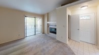 This single-story residence at Santa Lucia offers a thoughtfully arranged 1-bedroom, 1-bathroom layout designed for comfortable everyday living. The living room serves as the heart of the unit, featuring plush carpeted flooring, a tile-surround fireplace as a focal point, and a sliding glass door that opens to a private patio, allowing natural light to flow into the space.

The kitchen is positioned just off the living area and is defined by a raised peninsula counter with dark speckled countertops, warm honey-toned wood cabinetry, and pendant lighting overhead. The kitchen includes a range, refrigerator, and built-in microwave, with tile flooring that extends throughout the cooking space.

The bedroom is generously proportioned with soft carpeting, a ceiling fan, and a window fitted with blinds that provides natural light and outdoor views. The full bathroom is well-equipped, featuring an extended vanity with dark countertops and wood cabinetry, a large mirror with overhead lighting, and a shower-tub combination with sliding glass doors and wood-look tile flooring.

A dedicated in-unit laundry area accommodates a full-sized washer and dryer, adding everyday convenience. Neutral tones and consistent finishes throughout give the space a clean, cohesive feel.
