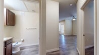 This single-floor residence offers a thoughtfully organized layout encompassing two bedrooms, two bathrooms, a kitchen, a hallway, and two closets. Throughout the unit, durable wood-look flooring in a warm gray-brown tone provides a cohesive aesthetic that flows from room to room.

The living area is finished with crown molding and a ceiling fan with integrated lighting, lending a polished appearance to the space. Natural light enters through blinds-fitted windows, brightening the neutral, beige-toned walls. The hallway connects the main living areas to the private quarters efficiently.

The galley-style kitchen features rich, dark-stained cabinetry paired with granite-style countertops and black appliances, including a refrigerator, range, and dishwasher, maximizing functionality within a compact footprint.

The primary bedroom accommodates a comfortable living arrangement and benefits from a ceiling fan and natural light. The second bedroom similarly includes a ceiling fan and window with blinds.

Both bathrooms are finished with dark wood vanity cabinetry and granite-style countertops. One bathroom features a soaking tub with tiled surround, while the second offers a walk-in glass-enclosed shower, providing practical options for residents.
