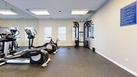 Located at 1300 Gran Crique Dr in Roswell, GA, this fitness center offers a dedicated exercise room designed to support a comprehensive workout routine. The space features durable rubber flooring throughout, providing a safe and resilient surface for all types of physical activity. Neutral gray walls and recessed panel lighting create a clean, focused environment conducive to exercise.

Natural light enters through multiple windows fitted with blinds, supplementing the overhead fluorescent panel lights and keeping the room bright and welcoming. A full-length mirror spans one wall, visually expanding the space and allowing users to monitor their form during workouts.

The room is equipped with a variety of cardio machines, including Life Fitness treadmills, elliptical trainers, and a spin bike, catering to a range of cardiovascular fitness needs. A multi-functional cable machine and pull-up station provide options for strength and resistance training, while a set of dumbbells rounds out the free weight offerings. The room is accessed through a doorway that connects to an adjacent area, and a fire extinguisher is mounted near the entrance for safety. Overall, the fitness center delivers a practical, well-organized environment for residents seeking convenient access to exercise facilities.