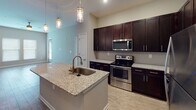 This single-story residence offers a thoughtfully designed open-concept layout that seamlessly connects the living area and kitchen. The living space features wood-style flooring and a ceiling fan, with large windows allowing natural light to fill the room. The kitchen is a standout feature, showcasing rich dark cabinetry that extends to the ceiling, granite countertops, a subway tile backsplash, and a full suite of stainless steel appliances including a range, microwave, and refrigerator. A central island with an undermount sink and pendant lighting above provides additional workspace and casual dining potential.

The bedrooms are carpeted for comfort, with multiple windows offering outdoor views and ceiling fans for climate control. One bedroom includes access to a walk-in closet. The primary bathroom features a walk-in shower, dark vanity cabinetry, granite countertops, and wood-style flooring. A secondary bathroom mirrors the design aesthetic and includes a tub-shower combination. Neutral gray walls throughout create a cohesive, modern feel across all spaces.