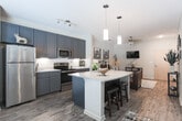 Located at 521 Fifth St in Macon, Georgia, this single-story unit offers a thoughtfully designed open-concept layout that seamlessly connects the kitchen, dining, and living areas. Wood-look flooring runs throughout, providing a cohesive and contemporary foundation across all spaces.

The kitchen is a standout feature, showcasing slate-blue shaker-style cabinetry extending to the ceiling, complemented by a white subway tile backsplash and light granite countertops. Stainless steel appliances—including a refrigerator, range, and built-in microwave—add a polished finish. A large central island with a granite surface, an undermount sink, and bar seating serves as a functional and social hub, illuminated by dual pendant lights overhead.

The living area is generously proportioned, offering comfortable space for multiple seating arrangements. A ceiling fan provides climate comfort, and the neutral wall tones create a bright, welcoming ambiance.

The bedroom features large windows that allow abundant natural light and exterior views, contributing to an airy feel. Wood-look flooring continues here, maintaining design consistency.

The bathroom includes a full tub-shower combination, granite-topped vanity with navy cabinetry, and wood-look tile flooring, rounding out a well-finished and functional space.