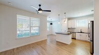 Located at 2403 Mall Dr in North Charleston, SC, this thoughtfully designed 2-bedroom, 2-bathroom residence offers a clean, modern aesthetic across a single floor. The open-concept living and kitchen area serves as the heart of the home, featuring light wood-style flooring, white walls, and a ceiling fan that enhances airflow and comfort. The kitchen is well-appointed with white shaker cabinetry, dark countertops, a subway tile backsplash, stainless steel appliances, and a central island with pendant lighting — ideal for both cooking and casual dining. Natural light fills the living area through large windows with blinds. A bright entrance hallway with recessed lighting and paneled doors connects the main living spaces to the private quarters. Both bedrooms are carpeted, equipped with ceiling fans, and receive natural light through windows. The primary bedroom connects to a bathroom featuring accessibility grab bars, a vanity with dark countertops, and wood-style flooring. The second bathroom offers a full tub-shower combo, a framed mirror, dark countertop vanity, and matte black fixtures throughout. Two closets provide ample storage, completing this well-organized and move-in-ready residence.