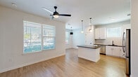 Located at 2403 Mall Dr in North Charleston, SC, this thoughtfully designed 2-bedroom, 2-bathroom residence offers a clean, modern aesthetic across a single floor. The open-concept living and kitchen area serves as the heart of the home, featuring light wood-style flooring, white walls, and a ceiling fan that enhances airflow and comfort. The kitchen is well-appointed with white shaker cabinetry, dark countertops, a subway tile backsplash, stainless steel appliances, and a central island with pendant lighting — ideal for both cooking and casual dining. Natural light fills the living area through large windows with blinds. A bright entrance hallway with recessed lighting and paneled doors connects the main living spaces to the private quarters. Both bedrooms are carpeted, equipped with ceiling fans, and receive natural light through windows. The primary bedroom connects to a bathroom featuring accessibility grab bars, a vanity with dark countertops, and wood-style flooring. The second bathroom offers a full tub-shower combo, a framed mirror, dark countertop vanity, and matte black fixtures throughout. Two closets provide ample storage, completing this well-organized and move-in-ready residence.