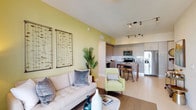 This single-floor residence offers a well-designed open-concept layout that seamlessly connects the living, dining, and kitchen areas. The living room is highlighted by warm yellow-green accent walls, track lighting, and a sliding glass door that opens to a private balcony with outdoor views, filling the space with natural light. Decorative wall art and a mix of neutral and accent furnishings contribute to a contemporary, inviting ambiance.

The kitchen is outfitted with light wood-grain cabinetry extending to the ceiling, granite countertops, a white subway tile backsplash, and a full suite of stainless steel appliances including a refrigerator, electric range, built-in microwave, and dishwasher. A freestanding island with bar-height seating provides additional workspace and casual dining.

Both bedrooms are generously sized, each with access to a balcony and ample closet storage. The primary bedroom features a walk-in closet with multi-level wire shelving. Both bathrooms include granite-topped vanities with modern cabinetry, large mirrors, and tile flooring. One bathroom offers a tub-shower combination, while the other includes a shower and a bright window for natural ventilation.