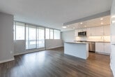 Located at 3620 Kaneff Crescent in Mississauga, Ontario, this well-appointed one-bedroom, one-bathroom unit offers a thoughtfully designed open-concept layout finished with light-toned laminate hardwood flooring throughout. The combined kitchen and living area forms the heart of the unit, anchored by a sleek, modern kitchen featuring high-gloss white cabinetry extending to the ceiling, a white subway tile backsplash, quartz countertops, stainless steel appliances including a built-in range, microwave, and refrigerator, and a central island that provides additional prep and dining space. Recessed pot lighting illuminates the kitchen area, enhancing its clean, contemporary aesthetic. The living area flows naturally from the kitchen and is bathed in natural light through a full-width floor-to-ceiling sliding glass door and window wall, which opens to a balcony and frames views of the surrounding Mississauga cityscape. The spacious primary bedroom features neutral grey walls, large windows, and ample room for furnishing. The bathroom is finished with crisp white large-format wall tiles, a soaker tub with an overhead rain showerhead, and chrome fixtures, offering a clean and functional design. The unit presents a bright, modern, and efficiently organized living space.