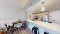 Located at 696 Whitney Rd W in Fairport, NY, this third-floor apartment offers a well-designed, single-level layout that maximizes both comfort and functionality. The open-concept living and dining area is bathed in soft, neutral tones with light sage-green walls and durable wood-look flooring that flows seamlessly throughout the main living spaces. A sliding glass door in the living area provides access to an outdoor balcony, allowing natural light to fill the room. The kitchen is efficiently designed with light maple cabinetry, stainless steel appliances including a refrigerator, electric range, and microwave, and a white countertop peninsula that doubles as a breakfast bar with pendant lighting overhead — ideal for casual dining or entertaining. The bedroom features plush carpeting, multiple windows with natural light, and ample space for a full furniture arrangement. The bathroom is finished with a wood-toned vanity, a large mirror with overhead lighting, and a walk-in shower with grab bar accessibility. Throughout the unit, clean lines, neutral palettes, and practical finishes create a calm, cohesive atmosphere well-suited for comfortable everyday living in the Fairport community.