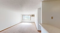 Located at 3415 Federal Dr in Eagan, Minnesota, this single-floor unit offers a functional and straightforward layout suited for comfortable everyday living. The spacious living area is finished with light-toned wall-to-wall carpeting, white walls, and a textured ceiling, and is filled with natural light streaming through a large window dressed with vertical blinds. A baseboard heating system and wall-mounted AC unit ensure year-round climate control. The kitchen is well-appointed with warm oak cabinetry offering generous storage, light-colored countertops, tile flooring, and white appliances including an electric range, dishwasher, and refrigerator. A pass-through counter connects the kitchen to the living area, enhancing the open feel of the space. The bedrooms continue the carpeted aesthetic, each featuring white walls, wood-trimmed doors, and windows that allow ample natural light. One bedroom includes mirrored sliding closet doors. The full bathroom is finished with tile flooring, a wooden vanity with a countertop sink, and a tub-shower combination. Overall, the unit presents a clean, neutral palette with a practical layout throughout.