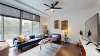 This thoughtfully designed single-floor studio offers an efficient and stylish layout across a compact footprint. The open-concept living and kitchen area serves as the heart of the space, where rich hardwood flooring flows seamlessly throughout, creating a warm and cohesive aesthetic.

The living area is bright and inviting, anchored by a large window fitted with a roller shade that allows for adjustable natural light and views of the surrounding urban environment. Elevated ceilings give the space an airy, loft-like quality, further enhanced by a modern ceiling fan with integrated lighting. Clean white walls provide a neutral backdrop that complements the contemporary design.

The kitchen is well-appointed and functional, featuring two-tone cabinetry with white upper cabinets and slate-blue lower cabinets, white subway tile backsplash, light countertops, and a full suite of stainless steel appliances including a refrigerator, electric range, and over-the-range microwave. Hardwood flooring continues into this space, maintaining visual continuity throughout.

The bathroom offers a clean, minimalist design with a full soaking tub and shower combination enclosed by crisp white subway tile walls and chrome fixtures, complemented by a light curtain for a fresh, airy feel. Overall, this studio combines urban functionality with modern design sensibilities.