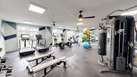 Located at 527 Herndon Square Ave in Atlanta, GA, this fitness center offers a thoughtfully designed exercise space that caters to a wide range of workout preferences. The single-floor layout provides a generous, open floor plan finished with durable speckled rubber flooring ideal for high-activity use.

The room is defined by its striking geometric wall mural, featuring bold navy blue diagonal shapes against a light gray-blue background, lending the space a modern and energetic aesthetic. Large windows along the perimeter flood the room with natural light and offer views of the surrounding neighborhood, while ceiling fans and recessed skylight panels ensure comfortable ventilation and even illumination throughout.

A full wall of floor-to-ceiling mirrors expands the sense of space and supports proper form during workouts. The cardio section is well-appointed with treadmills, elliptical trainers, stationary bikes, and a rowing machine. A dedicated free weights area features a multi-tiered dumbbell rack alongside adjustable benches, while a cable machine and punching bag cater to strength and functional training. Stability balls and a posted exercise guide round out the functional fitness offerings.

The overall ambiance is clean, bright, and motivating, combining practical equipment variety with an intentional, modern design sensibility.