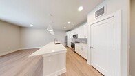This single-floor unit showcases a clean, contemporary design highlighted by light wood-tone flooring and neutral warm-beige walls throughout. The open-concept kitchen serves as the centerpiece, featuring crisp white shaker cabinetry with brushed nickel hardware, a light gray subway tile backsplash, and a full suite of stainless steel appliances including a refrigerator, range, and built-in microwave. A generously sized white quartz island with an integrated sink anchors the space, illuminated by a trio of modern pendant lights overhead, while recessed lighting provides additional brightness throughout.

The living area is well-proportioned and bathed in natural light from a set of French doors flanked by windows, offering outdoor views and fitted with blinds. A ceiling fan adds functionality to this open space. Bedrooms are comfortably sized, each featuring natural light from windows with blinds and ceiling fans. One bedroom benefits from dual windows, enhancing airflow and brightness.

The bathroom is well-appointed with a white shaker vanity, quartz countertop, brushed nickel fixtures, a large framed mirror, and a tub-shower combination. A dedicated laundry area and in-unit entry door with a keypad lock round out this well-designed space.