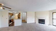 Located at 100 Hunt Club Dr in Copley, Ohio, this well-appointed two-bedroom, two-bathroom residence offers a functional single-floor layout. The open-concept living and dining area is highlighted by a tile-surround fireplace and a sliding glass door that leads to a private balcony with pleasant outdoor views, allowing natural light to fill the space. Soft carpet underfoot adds warmth to the living area and bedrooms.

The galley-style kitchen features warm wood cabinetry, granite-look countertops, a stainless steel sink, a dishwasher, electric range, and a refrigerator. A raised peninsula counter separates the kitchen from the living area, providing additional prep and serving space. Dark hardwood-style flooring grounds the kitchen and flows into the laundry room, which is equipped with a utility shelf, electrical panel access, and a fire extinguisher.

Both bedrooms are carpeted and offer ample wall space, with the primary bedroom including a generously sized walk-in closet outfitted with built-in shelving and dual hanging rods. The bathrooms feature granite-look vanity countertops, a large mirror, classic tile flooring with a decorative pattern, and a tub/shower combination. A hallway connects all rooms, contributing to a clear and efficient floor plan throughout.