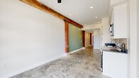 This one-bedroom, one-bathroom unit blends industrial character with modern finishes throughout its efficiently designed single-floor layout. Polished concrete floors run continuously through the entire space, lending a cohesive, urban aesthetic that complements the unit's raw architectural elements.

The open living area is defined by striking exposed reclaimed wood beams and bold red structural columns that reference the building's historic origins. A sage green accent wall adds a touch of warmth and color contrast against the crisp white walls and ceilings, which are fitted with recessed lighting throughout.

The kitchen is well-appointed with white shaker-style cabinetry extending to the ceiling for ample storage, dark countertops, a subway tile backsplash, and a full suite of stainless steel appliances including a refrigerator, dishwasher, microwave, and range.

The bedroom is a cozy yet functional space featuring an exposed brick wall with a window that brings in natural light, a sliding barn door rail, a closet, and a reclaimed wood beam overhead—continuing the industrial design language found throughout the unit.

The bathroom maintains the same clean aesthetic with white cabinetry, dark countertops, and polished concrete-style flooring. A hallway connects the rooms, providing a clear and practical flow through the space.