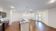This well-appointed 2-bedroom, 2-bathroom single-story residence in Austin, TX offers a thoughtfully designed open-concept layout. The combined kitchen and living area serves as the heart of the home, featuring rich hardwood-style flooring, recessed lighting, and a ceiling fan that enhances airflow and comfort. The kitchen is equipped with dark cabinetry, granite countertops, a central island with a double-basin sink, pendant lighting, and black appliances including a refrigerator and range. The living area is bright and airy, benefiting from natural light through multiple windows and a set of French doors that open to the outdoors. Both bedrooms are carpeted and finished in neutral tones, providing a calm retreat. The primary bedroom includes a spacious walk-in closet outfitted with built-in shelving, hanging rods, and additional storage cubbies. The bathrooms feature granite-topped dark vanities, hardwood-style flooring, and a tub-shower combination. A hallway connects the private quarters to the main living spaces, with a closet providing additional storage. The clean, modern aesthetic and functional layout make this residence a practical and comfortable home in Austin.
