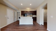 Located at 700 Reynoldsburg New Albany Rd in Blacklick, Ohio, this single-floor residence offers a well-designed layout that balances functionality and comfort throughout. The open-concept living and kitchen area serves as the heart of the home, finished with rich, dark hardwood-style flooring that extends seamlessly throughout the main living spaces. The kitchen is appointed with dark espresso cabinetry extending to the ceiling, light granite-style countertops, black appliances including a refrigerator, microwave, and range, and a central island with bar seating — ideal for both meal preparation and casual dining. A dedicated pantry with built-in shelving provides ample storage directly off the kitchen. The bedrooms feature neutral-toned carpet, natural light from well-placed windows, and generous closet space, including a large walk-in closet outfitted with wire shelving on multiple walls. The bathrooms are finished with large-format tile flooring and include a walk-in shower with sliding glass doors in one bath, along with grab bars for added accessibility. Warm beige tones throughout the walls create a cohesive and inviting atmosphere across all rooms, making this a practical and comfortable single-level living space.