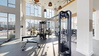 Located at 7000 Kiran Patel Dr in Winter Garden, Florida, this expansive fitness center offers a generously proportioned, single-floor layout designed to accommodate a full range of exercise activities. The space makes an immediate impression with its dramatic double-height ceilings and floor-to-ceiling glass walls that flood the interior with natural light and offer open views of the surrounding outdoor areas, including a pool and landscaping.

The main exercise floor features durable speckled rubber flooring and is outfitted with a comprehensive selection of strength training equipment, including multi-station cable machines, free weight racks stocked with dumbbells and kettlebells, adjustable benches, and a variety of resistance machines. Cardio equipment, such as stair climbers and stationary bikes, is thoughtfully positioned near the expansive windows to take advantage of the natural light and outdoor views.

Warm wood-paneled accent walls add a refined, contemporary touch to the otherwise clean, white interior. Large ceiling fans and pendant lighting complement the bright, airy atmosphere. A separate studio room with light hardwood flooring, full-wall mirrors, and linear ceiling lighting provides an ideal space for yoga, stretching, or group fitness classes. Glass-panel doors connect the studio to the main workout floor, maintaining visual openness throughout the entire facility.