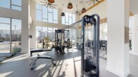 Located at 7000 Kiran Patel Dr in Winter Garden, Florida, this expansive fitness center offers a generously proportioned, single-floor layout designed to accommodate a full range of exercise activities. The space makes an immediate impression with its dramatic double-height ceilings and floor-to-ceiling glass walls that flood the interior with natural light and offer open views of the surrounding outdoor areas, including a pool and landscaping.

The main exercise floor features durable speckled rubber flooring and is outfitted with a comprehensive selection of strength training equipment, including multi-station cable machines, free weight racks stocked with dumbbells and kettlebells, adjustable benches, and a variety of resistance machines. Cardio equipment, such as stair climbers and stationary bikes, is thoughtfully positioned near the expansive windows to take advantage of the natural light and outdoor views.

Warm wood-paneled accent walls add a refined, contemporary touch to the otherwise clean, white interior. Large ceiling fans and pendant lighting complement the bright, airy atmosphere. A separate studio room with light hardwood flooring, full-wall mirrors, and linear ceiling lighting provides an ideal space for yoga, stretching, or group fitness classes. Glass-panel doors connect the studio to the main workout floor, maintaining visual openness throughout the entire facility.