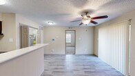 This well-designed single-floor unit offers a thoughtful layout that maximizes every square foot of its compact footprint. The open-concept living and kitchen area serves as the heart of the home, featuring light wood-look hard flooring, a textured ceiling, and a ceiling fan that provides both style and airflow. Vertical blinds cover a sliding door, allowing for adjustable natural light in the living space.

The kitchen is equipped with rich dark wood cabinetry, a mosaic tile backsplash, black appliances including a refrigerator, range, and dishwasher, and a clean white countertop peninsula that doubles as a breakfast bar. A dedicated laundry hookup area adds everyday convenience.

The bedroom is a comfortable retreat carpeted in neutral tones, with two windows dressed in horizontal blinds that bring in natural light and offer outdoor views of greenery. A closet provides additional storage.

The bathroom features a tiled tub-and-shower combination with a decorative mosaic tile border, grab bars, and a wall-mounted toilet, reflecting a clean and functional design. Throughout the unit, warm beige walls and consistent flooring choices create a cohesive, neutral aesthetic that is both practical and move-in ready.