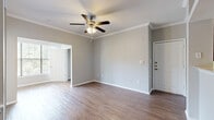 This efficiently designed single-floor residence offers a thoughtful layout across one bedroom, one bathroom, and multiple hallways and closets. The open-concept living and kitchen area forms the heart of the home, where rich hardwood-style flooring, crown molding, and neutral gray walls create a clean, modern aesthetic. The kitchen features dark espresso cabinetry, granite-look countertops, a breakfast bar peninsula, stainless steel appliances, and track lighting overhead. The adjacent living room is generously sized, complete with a ceiling fan and access to the entryway, maintaining an easy flow throughout the space. The bedroom is a comfortable retreat, carpeted for warmth and outfitted with crown molding, two large windows that invite ample natural light and outdoor views, and double doors that open to the bathroom. The bathroom is well-appointed with a dark wood vanity, stone-finish countertop, tile flooring, and a large mirror. Two closets provide practical storage throughout the unit. Hallways connect the spaces efficiently, and the overall palette of soft grays, warm wood tones, and white trim lends the residence a cohesive, move-in-ready character.