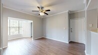 This efficiently designed single-floor residence offers a thoughtful layout across one bedroom, one bathroom, and multiple hallways and closets. The open-concept living and kitchen area forms the heart of the home, where rich hardwood-style flooring, crown molding, and neutral gray walls create a clean, modern aesthetic. The kitchen features dark espresso cabinetry, granite-look countertops, a breakfast bar peninsula, stainless steel appliances, and track lighting overhead. The adjacent living room is generously sized, complete with a ceiling fan and access to the entryway, maintaining an easy flow throughout the space. The bedroom is a comfortable retreat, carpeted for warmth and outfitted with crown molding, two large windows that invite ample natural light and outdoor views, and double doors that open to the bathroom. The bathroom is well-appointed with a dark wood vanity, stone-finish countertop, tile flooring, and a large mirror. Two closets provide practical storage throughout the unit. Hallways connect the spaces efficiently, and the overall palette of soft grays, warm wood tones, and white trim lends the residence a cohesive, move-in-ready character.