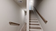 This three-story residence offers a thoughtfully organized layout across three distinct floors, each contributing its own functional purpose to the home. The ground floor features an attached garage with an automatic opener, a utility room housing the water heater and mechanical systems, and a hallway providing interior access — all finished with clean, neutral-toned walls and concrete flooring.

The main living level hosts a combined kitchen and living room, where light hardwood-style flooring flows throughout. The kitchen is appointed with white shaker cabinetry, stainless steel appliances including a French door refrigerator, a built-in microwave, and an electric range, complemented by a large center island with a sink and light quartz countertops. A ceiling fan and sliding glass door bring natural light into the living area.

The upper floor accommodates all three bedrooms and three full bathrooms. The primary bedroom features a walk-in closet with wire shelving and carpet flooring, alongside a ceiling fan and windows with exterior views. Secondary bedrooms are carpeted and similarly bright, each with ceiling fans and window treatments. The bathrooms are finished with light hardwood-style flooring, white vanities, and tub-shower combinations. Multiple staircases with wood-toned treads and warm handrails connect all three levels seamlessly.