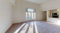 This single-floor residence offers a thoughtfully designed layout that balances open living spaces with practical functionality. The living area is a standout, featuring dramatically high ceilings that amplify the sense of space, plush carpeted flooring, and a set of large French doors that flood the room with natural light and open to views of the surrounding urban streetscape. The airy, neutral palette throughout creates a clean and welcoming atmosphere.

The bedrooms are generously proportioned, each finished with soft carpeting and large windows that frame views of the neighboring brick architecture. The elevated ceiling heights carry through these rooms, reinforcing the spacious feel. One bedroom features a direct en-suite connection, adding a layer of convenience and privacy.

The kitchen is designed in a compact galley configuration, efficiently utilizing its layout with ample white cabinetry extending to the ceiling, a mosaic tile backsplash, hardwood flooring, and a full suite of appliances including a full-size refrigerator. The countertops provide practical workspace alongside a stainless steel sink.

The bathroom is neatly appointed with a single vanity, mirror, tile flooring, and a full tub-shower combination, offering all essential amenities in a clean, well-maintained space.