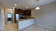 This single-floor residence is designed with an open-concept layout that promotes a seamless flow between the kitchen and adjacent living areas. The kitchen is a standout feature, showcasing rich dark wood cabinetry that extends to the upper walls, offering generous storage space. The countertops are finished in granite with warm, earthy tones, providing both durability and aesthetic appeal. A peninsula with an integrated sink separates the kitchen from the dining and living areas, making it ideal for casual interaction and entertaining. Stainless steel appliances, including a refrigerator, microwave, and range, lend a modern, polished look to the space. Recessed lighting throughout the kitchen ensures bright, even illumination, while a pendant light fixture hangs gracefully above the peninsula, adding a touch of warmth. The flooring throughout is light-toned tile, which contrasts elegantly with the darker cabinetry and contributes to a clean, cohesive aesthetic. Neutral-toned walls complement the overall palette, creating a welcoming and versatile atmosphere. The open layout and thoughtful design elements combine to make this a functional and visually appealing living space.
