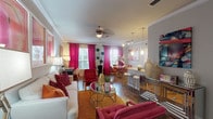 This single-floor residence makes a striking visual impression through its bold, cohesive use of color and carefully curated design elements throughout. The open-concept living and dining area serves as the heart of the home, where crown molding, hardwood-style flooring, and a ceiling fan lend architectural character. Vivid magenta drapery frames multiple windows, filling the space with natural light. The living area features a triptych of bold abstract artwork as a focal point above a cream sofa, complemented by a gold-accented glass coffee table. This flows seamlessly into a dining nook and a bar-height counter with pendant lighting — ideal for casual entertaining.

The galley-style kitchen is efficiently designed with dark cabinetry, granite countertops, tile flooring, and black appliances, with a direct sightline to an adjacent bathroom. A secondary room serves flexibly as a bedroom or home office, accented by vibrant artwork and magenta curtains. The bedrooms offer carpeted flooring, natural light from windows, and ample closet access. Both bathrooms include granite-topped dark wood vanities, framed mirrors, and tub-shower combinations, maintaining the home's warm, coordinated aesthetic throughout.