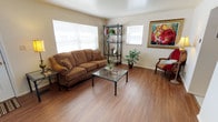 This two-story home offers a well-organized layout designed for comfortable everyday living. The living room serves as the heart of the main floor, featuring warm hardwood-style flooring, multiple windows fitted with blinds that allow natural light to fill the space, and enough room to accommodate generous seating arrangements. Decorative wall art adds character to the neutral-toned walls throughout.

Adjacent to the living area, the dining room provides a cozy setting for meals, equipped with a ceiling fan, a window overlooking the outdoors, and a wall-mounted mirror that enhances the sense of space. The kitchen is outfitted with warm wood cabinetry extending to the upper walls, a continuous countertop with an integrated sink, and standard appliances including a range and washer unit, offering practical functionality.

The upper level houses multiple bedrooms, each carpeted for comfort and brightened by windows with natural light. The bedrooms vary in size, accommodating different needs. The bathroom features classic white tile surrounding a full tub-shower combination, a wall-mounted vanity mirror, and a window providing ventilation and light. Throughout, the home maintains a clean, neutral palette that creates a calm and functional living environment.