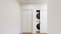 This well-designed two-bedroom, two-bathroom residence in Sheboygan, Wisconsin offers a clean, modern aesthetic across a single thoughtfully laid-out floor. The open-concept living and kitchen area serves as the heart of the home, anchored by a large central island with white quartz countertops and an undermount sink. Rich medium-toned cabinetry, stainless steel appliances, and a white subway tile backsplash complete the kitchen with a polished, contemporary look. Light hardwood flooring flows throughout the main living areas, adding warmth to the bright, neutral palette. The living area opens to a private balcony through sliding glass doors, framing open green field views that fill the space with natural light. Both bedrooms feature soft carpeting and generous closet space, with the primary bedroom benefiting from dual windows that continue the scenic outdoor views. The two bathrooms are finished with warm wood cabinetry, matte black hardware, white countertops, and light hardwood-style flooring. One bathroom includes a full soaking tub and shower combo. A conveniently tucked-away stacked washer and dryer unit adds in-unit laundry functionality. The hallway connects all spaces efficiently, completing this move-in-ready home.