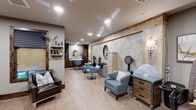 Located at 1196 T L Townsend Dr in Rockwall, Texas, this full-service salon and spa suite offers a cohesive blend of rustic warmth and contemporary design. The space is unified by light wood-look flooring, neutral gray walls, and rich dark-stained wood trim that frames mirrors, windows, and entryways throughout.

The main salon area features multiple styling stations equipped with professional chairs in soft blue upholstery, round wall-mounted mirrors, and dedicated dryer stations with rustic wood drawer units. A standout textured accent wall — framed in reclaimed-style lumber and adorned with decorative sconce lighting — anchors the styling area and adds depth and character to the interior.

A dedicated treatment room offers a padded treatment table, a professional styling chair, product shelving, and framed artwork, creating a calm and private environment for esthetic or spa services. A large interior window connects this room visually to the main salon floor.

The space also includes a pedicure station outfitted with a massage chair and foot basin, positioned near elegant glass-and-wood French doors that separate service areas while maintaining an open, airy feel. A nail polish display and comfortable seating complete this zone.

Recessed lighting throughout ensures a bright, welcoming atmosphere. The overall ambiance is polished yet approachable, making this salon suite a functional and aesthetically inviting professional environment.