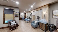 Located at 1196 T L Townsend Dr in Rockwall, Texas, this full-service salon and spa suite offers a cohesive blend of rustic warmth and contemporary design. The space is unified by light wood-look flooring, neutral gray walls, and rich dark-stained wood trim that frames mirrors, windows, and entryways throughout.

The main salon area features multiple styling stations equipped with professional chairs in soft blue upholstery, round wall-mounted mirrors, and dedicated dryer stations with rustic wood drawer units. A standout textured accent wall — framed in reclaimed-style lumber and adorned with decorative sconce lighting — anchors the styling area and adds depth and character to the interior.

A dedicated treatment room offers a padded treatment table, a professional styling chair, product shelving, and framed artwork, creating a calm and private environment for esthetic or spa services. A large interior window connects this room visually to the main salon floor.

The space also includes a pedicure station outfitted with a massage chair and foot basin, positioned near elegant glass-and-wood French doors that separate service areas while maintaining an open, airy feel. A nail polish display and comfortable seating complete this zone.

Recessed lighting throughout ensures a bright, welcoming atmosphere. The overall ambiance is polished yet approachable, making this salon suite a functional and aesthetically inviting professional environment.