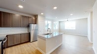 This single-floor residence offers a thoughtfully designed open-concept layout that seamlessly connects the kitchen, dining, and living areas. The kitchen serves as the heart of the home, featuring a central island with a granite countertop and integrated sink, rich dark-toned cabinetry, a full suite of stainless steel appliances including a refrigerator, electric range, and over-the-range microwave, and a classic subway tile backsplash. Recessed lighting illuminates the space, complementing the warm, light-toned hardwood flooring that extends throughout the entire residence. The open living area is bathed in natural light from multiple windows and is equipped with a ceiling fan for added comfort. A clean, well-lit hallway connects the main living spaces to the private areas of the home. The bedrooms are generously sized, each featuring ceiling fans, neutral-toned walls, and large windows fitted with horizontal blinds that allow for adjustable natural light. The bathroom is neatly appointed with a granite-topped vanity, a soaking tub with a tiled surround, and direct access to a walk-in closet. The overall ambiance of the space is modern, clean, and move-in ready, with a neutral color palette that provides a versatile backdrop for any interior style.