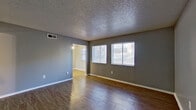 This single-story residence presents a cohesive design palette anchored by gray walls, white baseboards, and warm wood-style flooring that extends throughout the main living areas. The spacious living room is a central highlight, featuring dual windows fitted with blinds that invite natural light, a textured popcorn ceiling, and a ceiling-mounted HVAC vent for year-round comfort. An open passageway connects the living room to the galley-style kitchen, which is well-appointed with rich wood cabinetry, granite countertops, mosaic tile backsplash, and black appliances including a range and refrigerator. A ceiling fan with lighting is positioned at the kitchen's far end.

The bedrooms continue the consistent flooring and gray wall tones, with one room featuring a ceiling fan with light fixture and a walk-in closet. A sunroom-style bonus space is distinguished by horizontal shiplap-paneled walls and a mirrored sliding closet door, offering a unique retreat. The bathroom is well-equipped with a wide vanity topped in granite, a large framed mirror, built-in wall shelving, and a tub-shower combination with tile surround. Throughout, the unit maintains a clean, functional aesthetic.