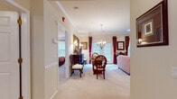 This single-floor residence offers a thoughtfully designed layout that seamlessly connects its principal living spaces. The living room serves as the heart of the home, featuring crown molding, recessed lighting, and plush carpeting. Large windows dressed with rich burgundy drapes flood the space with natural light, while French doors provide additional brightness. The adjoining dining area is anchored by an elegant chandelier, complementing the traditional aesthetic carried throughout.

The kitchen is outfitted with white cabinetry, dark granite countertops, stainless steel appliances including a gas range and refrigerator, and travertine tile flooring, offering both function and style. A breakfast bar with barstools adds casual dining versatility.

The generously sized bedroom features soft carpeting, recessed lighting, and a large window with natural light. Ample space accommodates a full furniture suite, with doors leading to a closet and the en-suite bathroom. The bathroom is finished in coordinating travertine tile on both the floors and walls, featuring a white vanity with a large mirror and a full soaking tub with shower combination. The overall ambiance is warm, classic, and cohesive throughout.