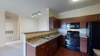 This single-story residence offers a cohesive layout with distinct living, kitchen, bedroom, and bathroom areas. The kitchen is a functional centerpiece, featuring rich dark-wood cabinetry, granite-style countertops, a double stainless steel sink, and black appliances including a gas range, built-in microwave, and dishwasher. Track lighting above the kitchen peninsula adds a modern touch, while crown molding throughout lends a polished, finished look. The kitchen flows openly toward the living area, which is finished with neutral-toned carpet and accented by crown molding, creating a comfortable and cohesive space.

The bedrooms are carpeted and bright, with multiple windows fitted with blinds allowing natural light to filter in. The primary bedroom includes a ceiling fan, two windows with outdoor views of greenery, and a walk-in closet with built-in shelving and hanging rods. The bathroom features hardwood-style flooring, dark-wood vanity cabinetry, and a tiled shower-tub combination with chrome fixtures. Throughout the unit, warm neutral wall tones and consistent finishes create a clean, unified aesthetic.