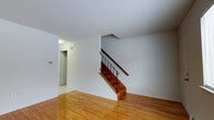 This two-bedroom, two-bathroom townhouse offers a functional and straightforward layout across two floors. The main level features warm hardwood flooring that extends throughout the living area, lending a classic and inviting character to the space. Clean white walls keep the interior bright and neutral, providing a versatile backdrop adaptable to various décor styles.

A staircase with wooden steps and a black metal railing serves as a central architectural element on the main floor, connecting the two levels in a clean, understated design. The staircase is positioned to allow the surrounding living area to feel open and unobstructed. Adjacent to the staircase, a hallway leads to additional rooms, including what appears to be a utility or storage area with its own door.

The upper floor houses the two bedrooms and bathrooms, offering separation between the living and sleeping areas — a hallmark of townhouse-style living. The overall ambiance of the home is clean and minimal, with a straightforward design that emphasizes practicality. The consistent use of hardwood flooring and neutral tones throughout creates a cohesive, easy-to-personalize environment suited for a variety of lifestyles.