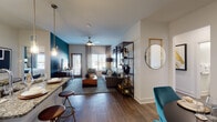 Located in Frisco, TX, this thoughtfully designed single-floor residence blends contemporary style with functional living. Rich hardwood-style flooring runs throughout, anchoring a cohesive design palette of deep teal accent walls, crisp white trim, and warm gold fixtures.

The open-concept living and dining area is bright and welcoming, featuring a ceiling fan, natural light from large windows with floor-length drapes, and a dedicated dining nook with built-in shelving. The kitchen is outfitted with stainless steel appliances, sleek white cabinetry, granite countertops, a tile backsplash, a deep undermount sink, and a breakfast bar with pendant lighting.

Two generously sized bedrooms each carry the home's signature teal accent walls and are complemented by ceiling fans and large windows offering outdoor views. The primary suite includes a walk-in closet and an en-suite bathroom with a glass-enclosed marble-tiled shower and granite vanity. A second bathroom features a full soaking tub with marble-surround tile and a decorative shower curtain.

Additional highlights include built-in display shelving, a dedicated dining area, and a cohesive design that balances bold color with refined, modern finishes throughout.