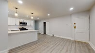 This thoughtfully renovated single-floor space presents a clean, modern aesthetic anchored by a cohesive neutral palette and light-toned luxury vinyl plank flooring that flows seamlessly throughout. The open-concept kitchen is a standout feature, showcasing crisp white shaker cabinetry with matte black hardware, a herringbone-patterned tile backsplash, and a full suite of stainless steel appliances including a gas range, built-in microwave, and dishwasher. A centered kitchen island with a bright white countertop provides additional workspace and serves as a natural divider between the kitchen and the generously sized living area. Recessed lighting and elegant pendant fixtures illuminate the space, enhancing its airy, welcoming feel. The living area offers ample room and is conveniently adjacent to a closet, providing practical storage. Two bedrooms continue the consistent design language, each featuring the same durable flooring and neutral grey walls, with windows that allow natural light to filter in. The full bathroom is finished with large-format grey tile flooring, a white vanity with a matte black faucet, a mirrored medicine cabinet, and a full soaking tub with shower — combining style and functionality in a well-appointed package.