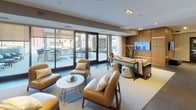 Located at 240 Chicago Ave in Minneapolis, MN, this single-floor amenity space is thoughtfully designed to offer residents a variety of social and recreational environments. The layout flows seamlessly across several distinct zones, each with its own character and function.

A bright, casual lounge area features built-in bench seating, round white pedestal tables, and contemporary upholstered chairs set atop neutral carpeting, with interior windows offering visual connectivity to adjacent spaces. A more refined sitting area showcases warm cognac leather armchairs, a central coffee table, and floor-to-ceiling glass doors that open directly onto an outdoor terrace equipped with seating and grilling stations.

The games and entertainment room is a standout feature, centered around a full-length shuffleboard table and anchored by dark leather sofas atop a decorative area rug. Recessed and cove lighting creates a dynamic ambiance, while large windows provide city views and multiple wall-mounted televisions enhance the entertainment experience.

A sophisticated bar and kitchen area offers an expansive white countertop with ample bar seating, pendant lighting above a gleaming mosaic tile backsplash, and integrated appliances. A cozy fireplace seating nook is visible nearby, adding warmth to the space. Together, these areas form a cohesive, upscale amenity floor suited for both relaxation and social gatherings.