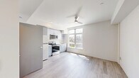 Located in the Derby neighborhood of Seattle, WA, this modern studio offers a thoughtfully designed open-concept layout that maximizes every square foot. Light-toned luxury vinyl plank flooring runs throughout, complementing the clean white walls and creating a bright, cohesive aesthetic.

The kitchen is a standout feature, outfitted with sleek gray cabinetry, open shelving, white countertops, and a full suite of stainless steel appliances including a refrigerator, electric range, over-the-range microwave, and sink. A large picture window positioned adjacent to the kitchen floods the living area with natural light and frames expansive views of the Seattle skyline and surrounding neighborhood rooftops. A ceiling fan overhead provides both comfort and a contemporary design touch.

The living area is open and versatile, offering a clean canvas with recessed lighting and a simple, modern entry door. The bathroom features wood-look flooring consistent with the rest of the unit, a vanity with storage, a toilet, and a walk-in shower with chrome fixtures. The overall design of this studio is clean, functional, and well-suited for urban living in one of Seattle's vibrant neighborhoods.