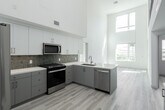 This contemporary townhouse in Irvine, CA offers 1200 square feet of living space across two floors. The ground floor spans 990 square feet, while the upper level adds 210 square feet. The home features three bedrooms, including a spacious 160 square foot primary bedroom, and three full bathrooms.

The interior showcases a modern aesthetic with high ceilings and an abundance of natural light streaming through large windows. Light-toned wood flooring runs throughout, complementing the crisp white walls and creating an airy ambiance. The kitchen boasts sleek cabinetry, stainless steel appliances, and a tasteful tile backsplash.

Bathrooms are outfitted with modern fixtures, including illuminated mirrors and ample storage. The property includes a walk-in closet for added convenience. An open-concept layout on the main floor promotes a sense of spaciousness, while the upper level features a loft-like area with stylish metal railings.

The townhouse also offers outdoor living space with a balcony, providing views of the surrounding area. Its location at 2055 Main St in Irvine puts residents in close proximity to urban amenities while maintaining a serene residential feel.