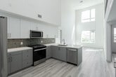Located at 2055 Main St in Irvine, CA, this contemporary two-story residence offers 2 bedrooms, 3 bathrooms, a loft, and a patio across two well-appointed floors. The main level is anchored by a dramatic open-concept kitchen and living area, distinguished by soaring double-height ceilings that flood the space with natural light. The modern kitchen features stainless steel appliances—including a gas range, dishwasher, and French door refrigerator—white quartz countertops, a subway tile backsplash, and sleek gray cabinetry with gold hardware. Light wood-style flooring runs throughout both levels, enhancing the bright, airy atmosphere. A patio off the main level provides outdoor access with urban views. Upstairs, the loft overlooks the living area below through a striking black metal railing, creating an open, connected feel. The primary bedroom is generously sized and accompanied by a well-appointed ensuite bathroom featuring a dual-sink vanity with a backlit mirror and gray cabinetry with gold accents. Additional bathrooms offer similar modern finishes with tub-shower combinations. Four closets, including walk-in options, provide ample storage throughout. The overall design is clean, minimalist, and move-in ready.